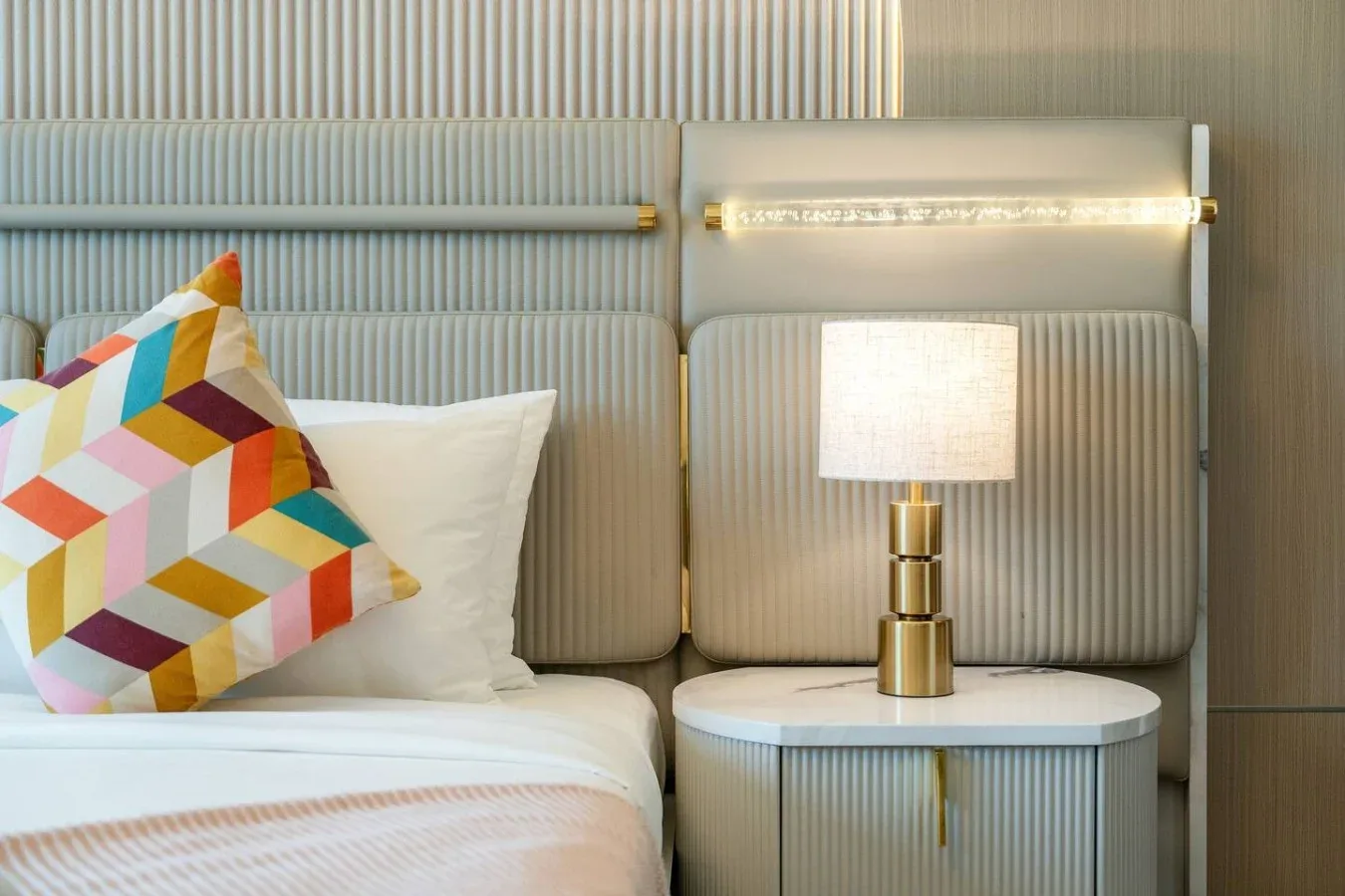 Dormitorio con cama, cojín geométrico de colores y mesita de noche.