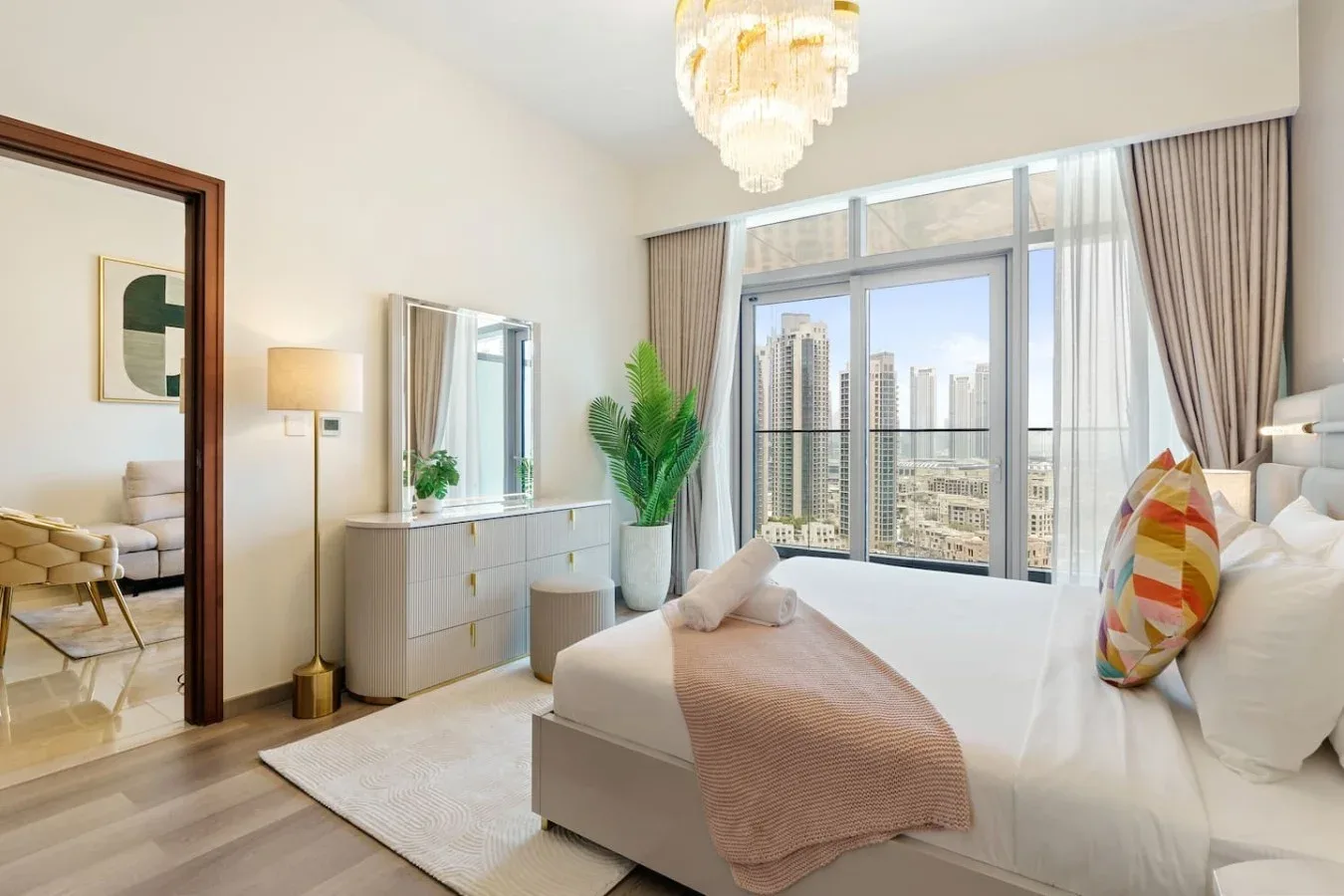 Un dormitorio luminoso con una cama junto a grandes ventanas con vistas a edificios de la ciudad.