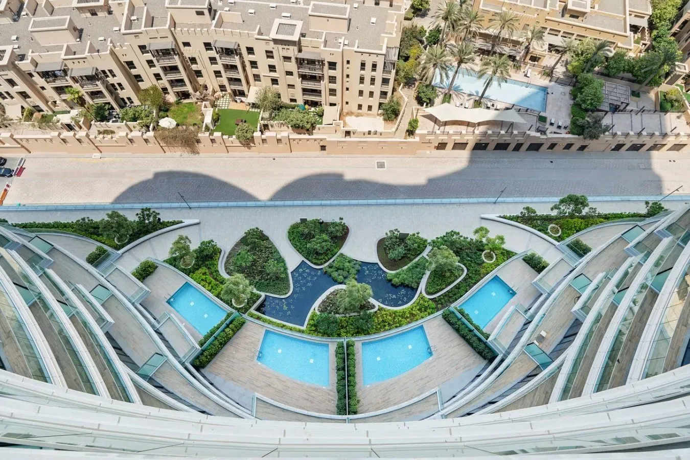 Vista aérea de un patio ajardinado con piscinas curvas entre edificios.