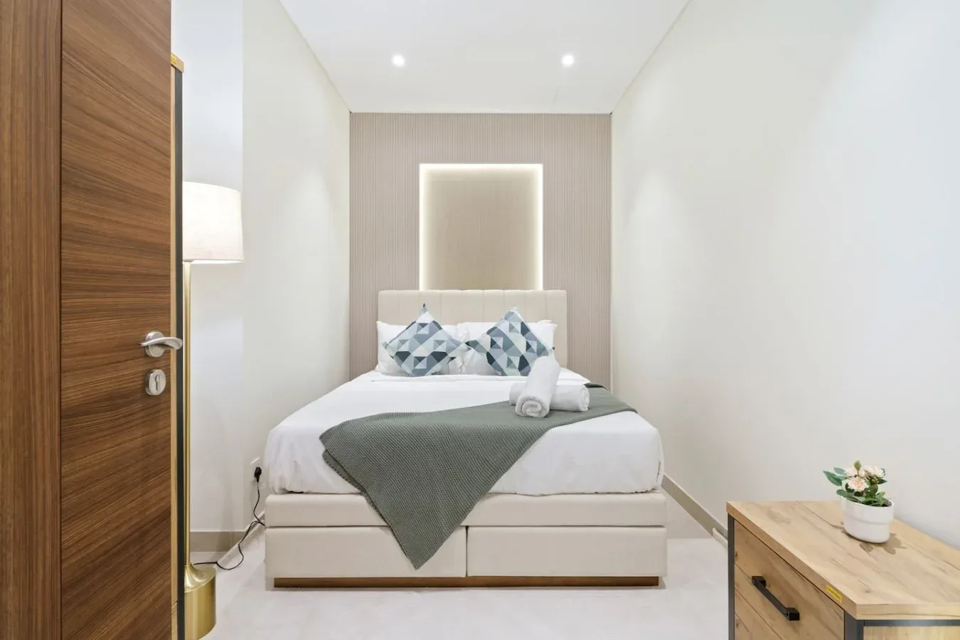 Un dormitorio con una cama tendida y una pequeña mesa de madera junto a ella.