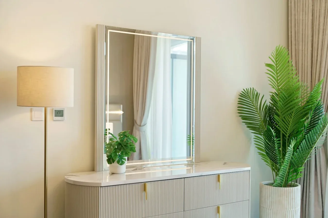 Una habitación luminosa con un espejo sobre una cómoda y plantas frondosas cerca.