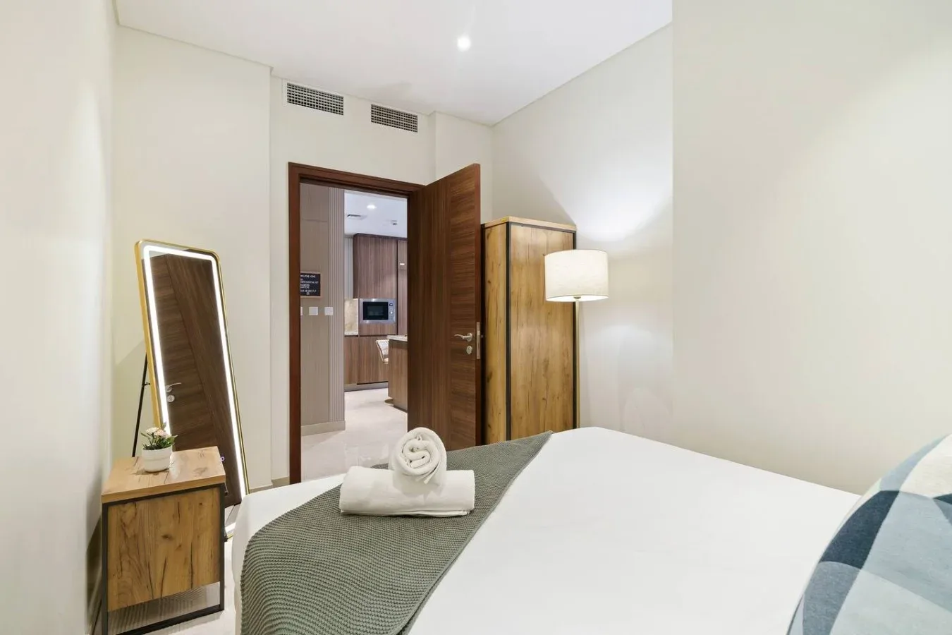 Un dormitorio con una cama ordenada, un espejo de cuerpo entero y una puerta abierta.