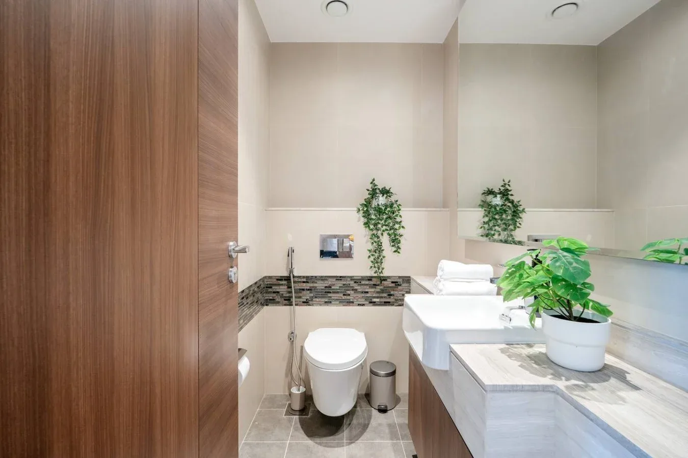 Un baño luminoso con inodoro, lavabo y plantas frondosas.