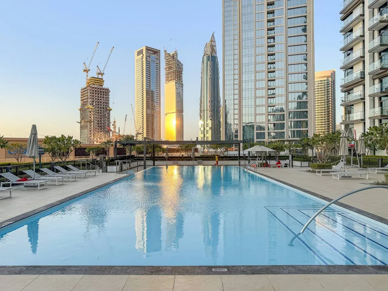 Una piscina al aire libre refleja los edificios altos circundantes con la luz del atardecer.
