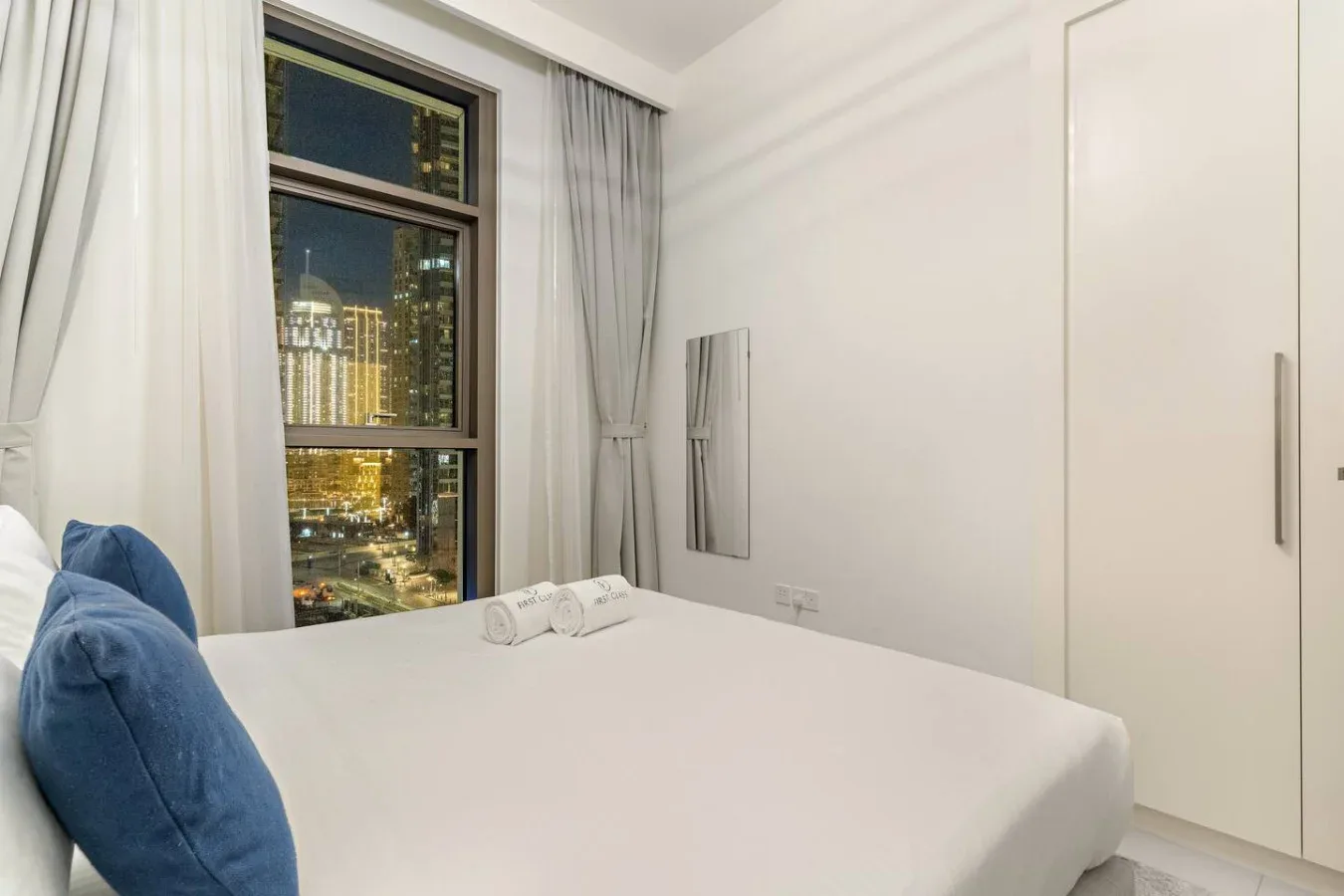 Un dormitorio con una cama junto a una ventana con vistas a luces de la ciudad por la noche.