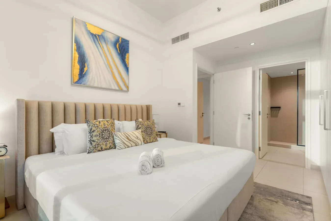 Un dormitorio luminoso con una cama bien tendida y arte abstracto colorido en la pared.