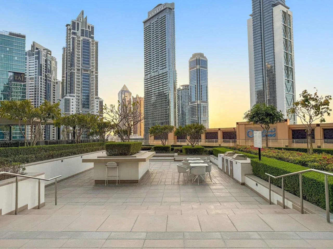 Una terraza pavimentada con asientos al aire libre ofrece vistas a varios edificios altos y modernos.