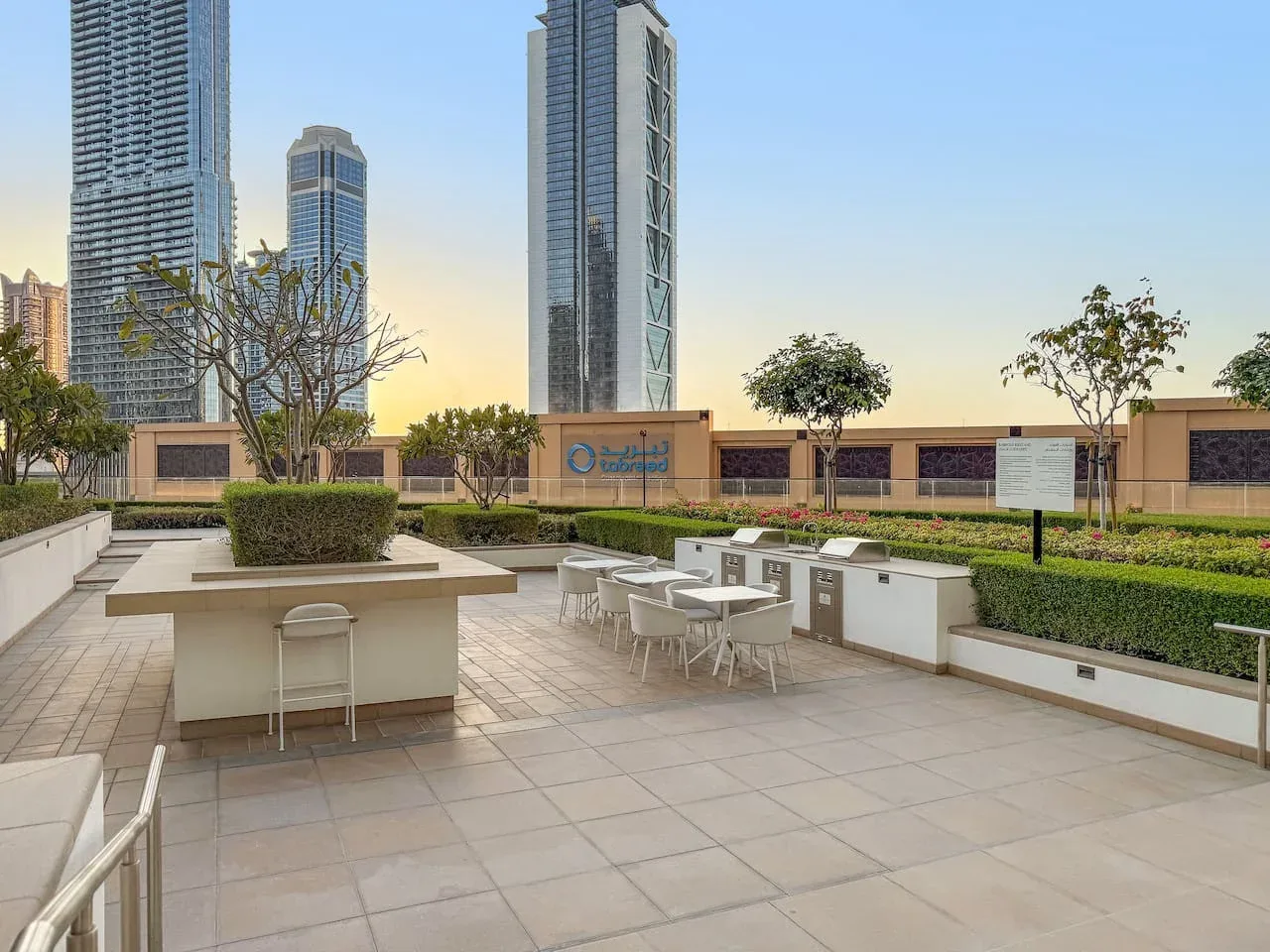 Una terraza exterior pavimentada con asientos, jardineras y edificios altos al fondo.