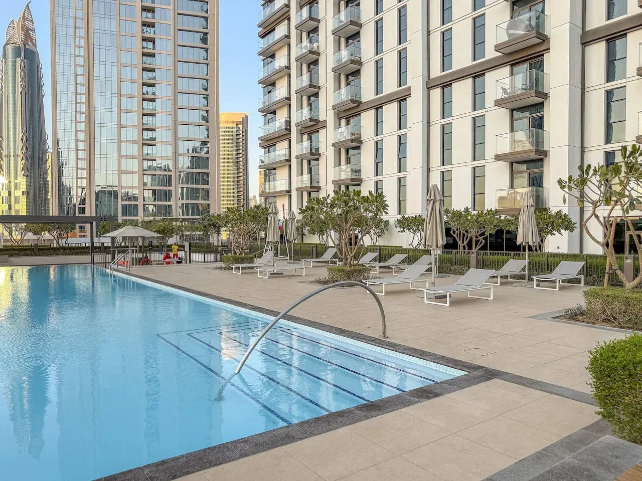 Una piscina al aire libre junto a un edificio moderno de gran altura y tumbonas.