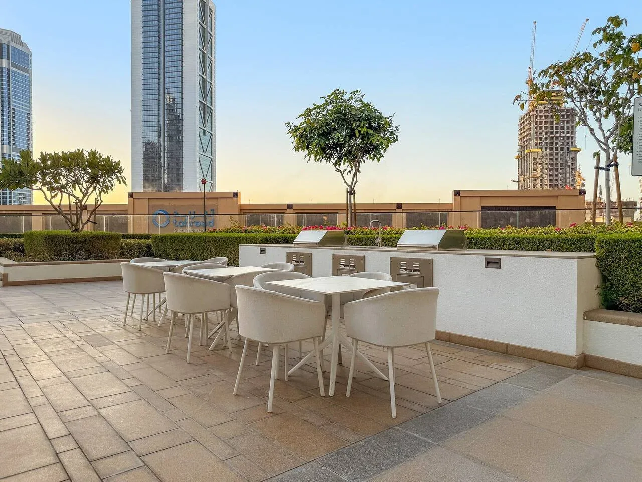 Una terraza al aire libre tiene asientos alrededor de mesas junto a una jardinera con plantas.