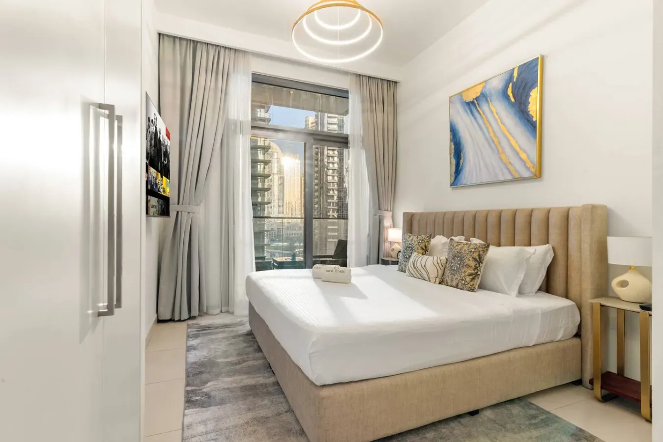 Un dormitorio luminoso con una cama grande, cortinas altas y vistas de la ciudad por la ventana.
