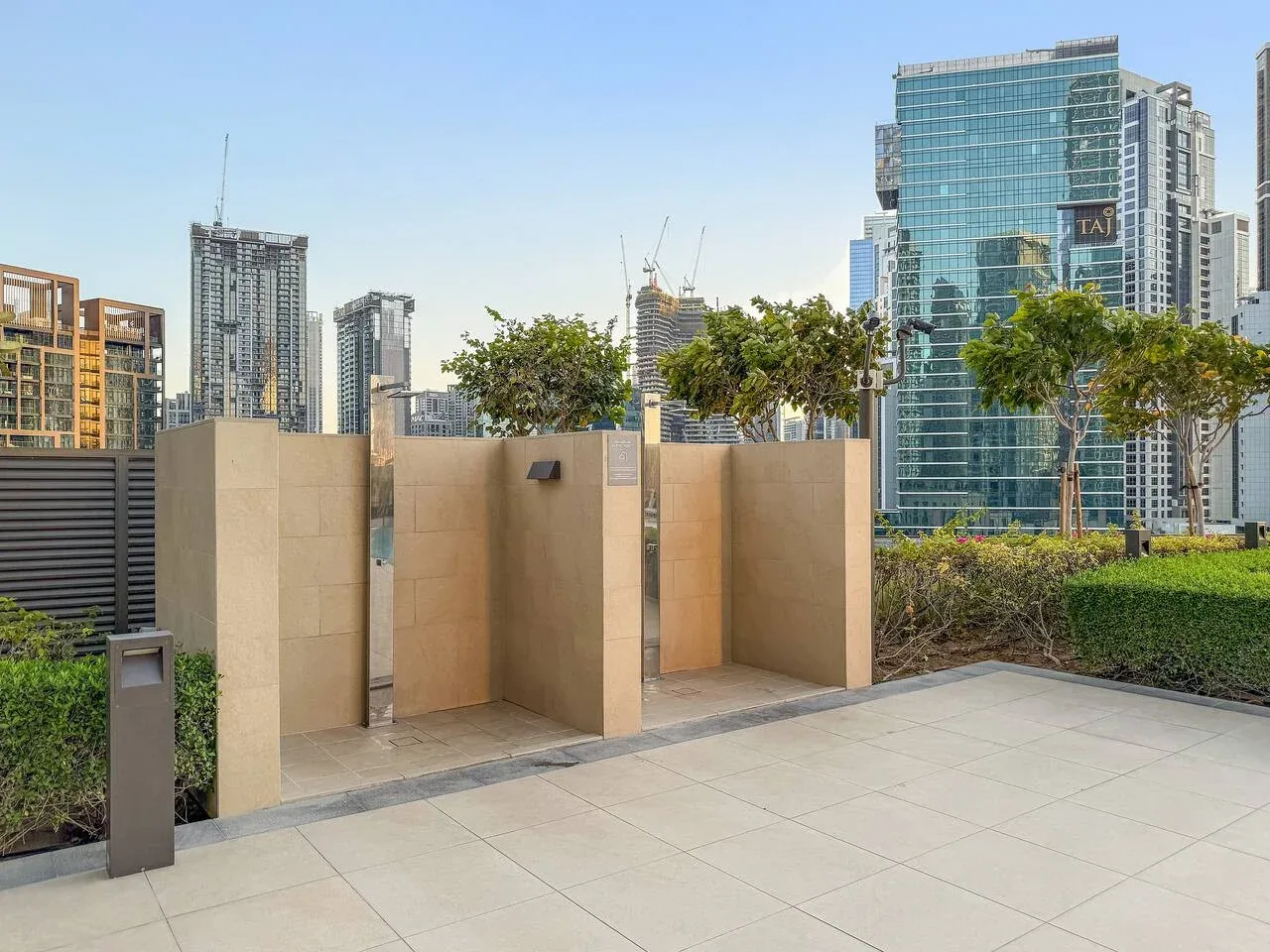 Terraza exterior pavimentada con muros beige, plantas y edificios altos al fondo.