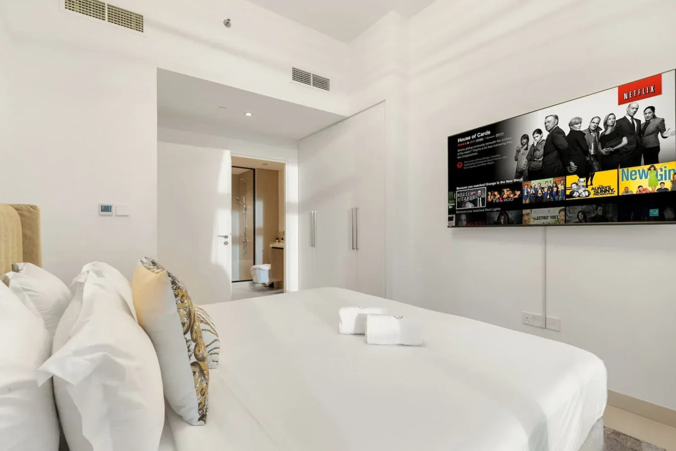 Un dormitorio luminoso con ropa de cama blanca y un televisor en la pared.