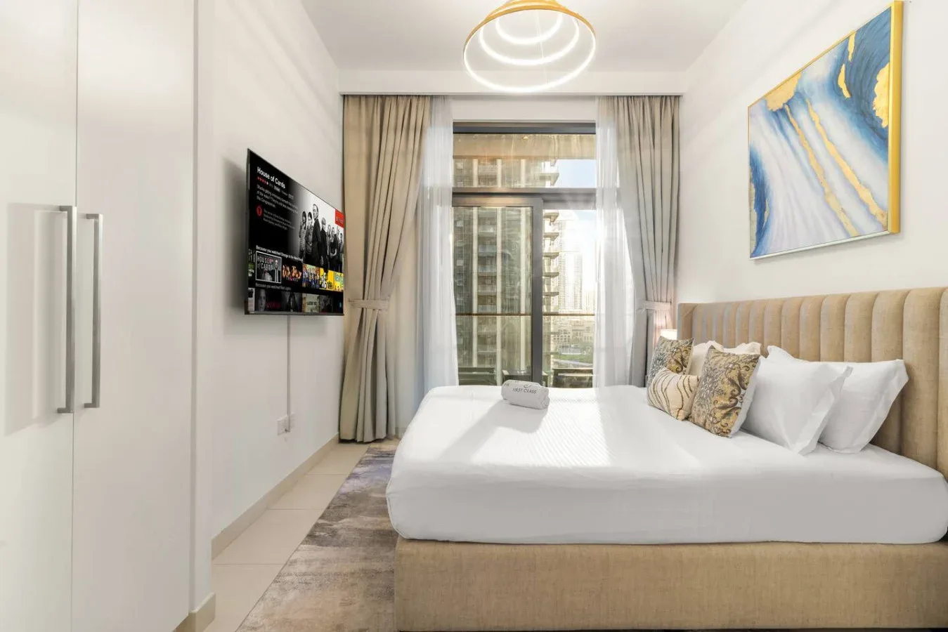 Un dormitorio luminoso con una cama arreglada junto a una ventana grande.