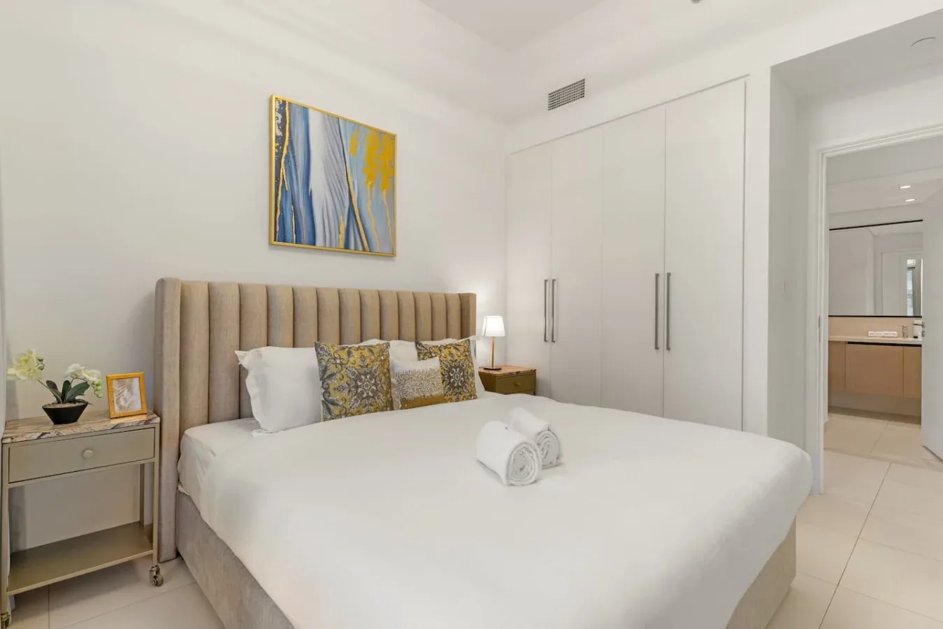 Un dormitorio luminoso con una cama bien tendida y arte abstracto en la pared.