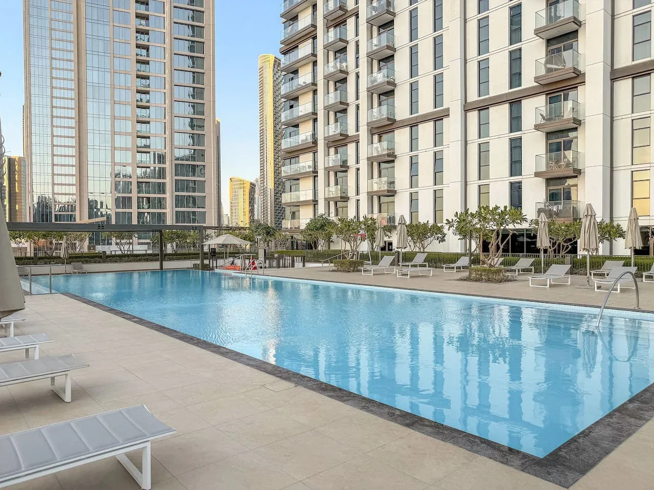 Una piscina al aire libre está junto a edificios altos modernos y asientos de descanso.