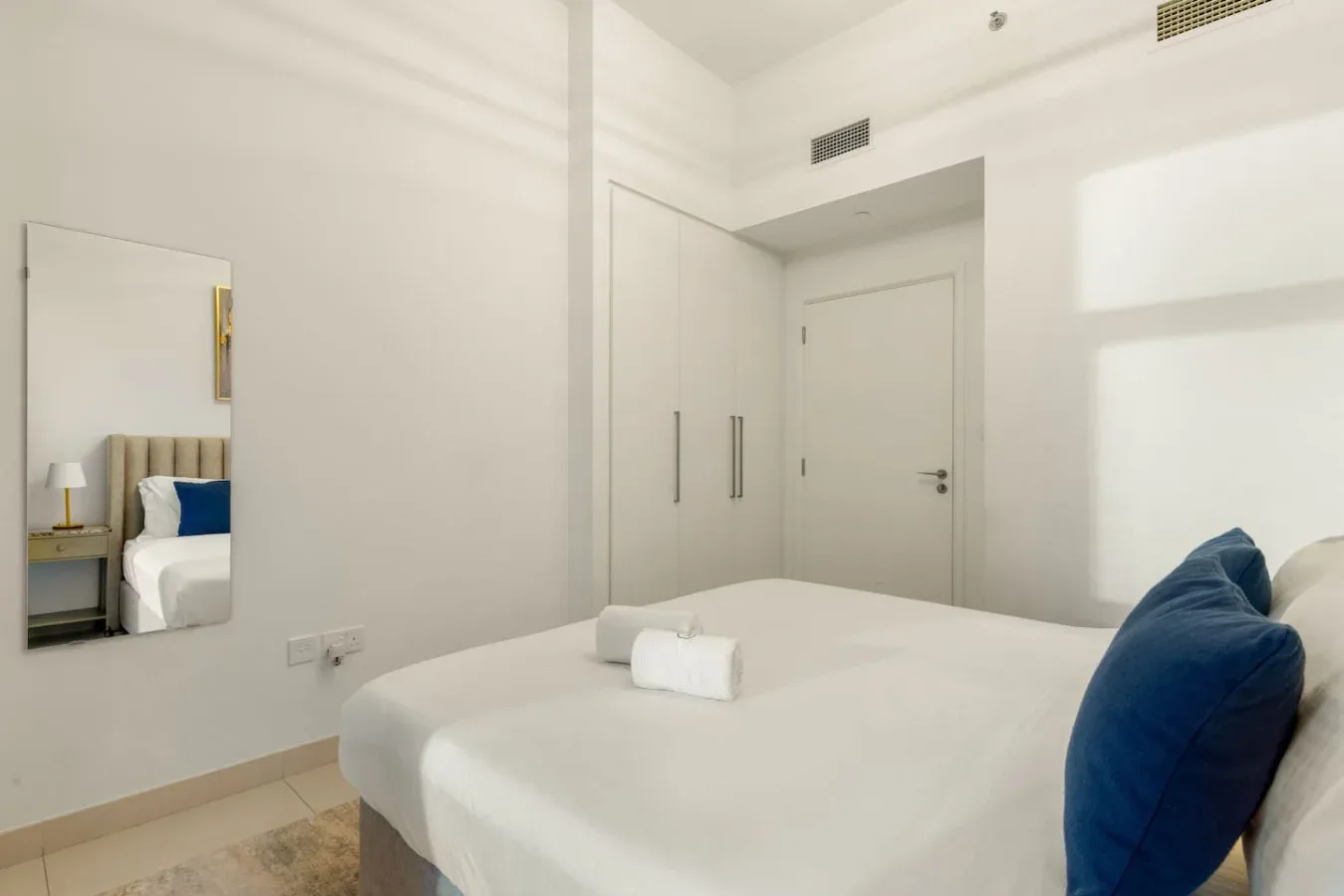 Un dormitorio luminoso con una cama bien hecha y almohadas azules.