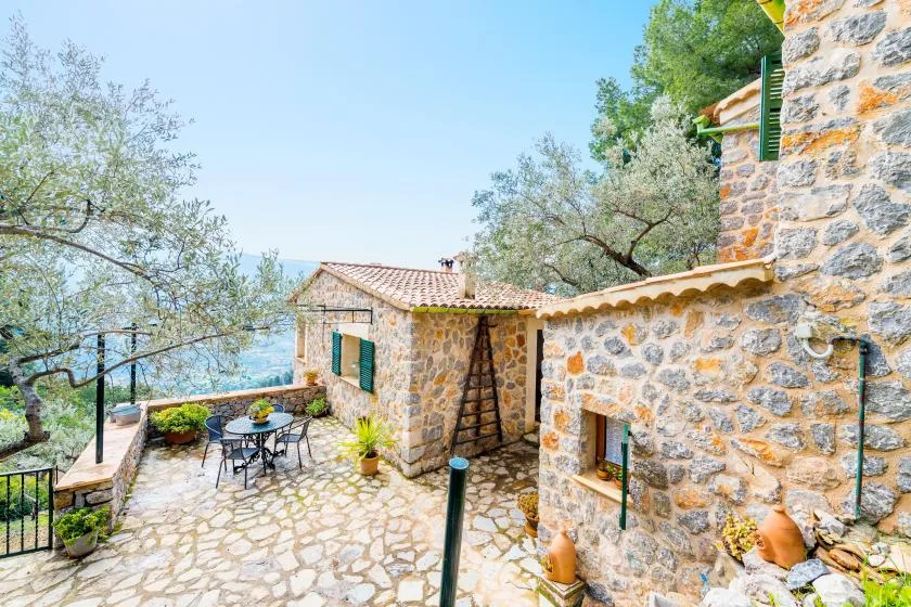 A stone courtyard with outdoor seating, potted plants, and views of the sea.