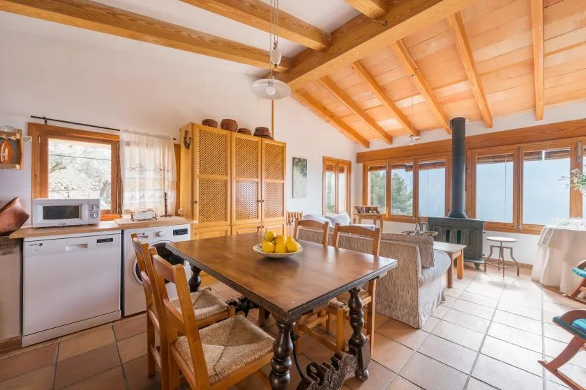 A bright dining and living area features a wooden table beside large windows.