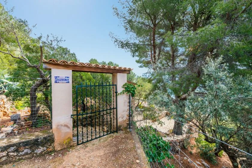A black metal gate stands between pale stucco pillars beneath a small tiled canopy.