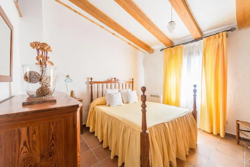 A bedroom with a wooden bed and yellow curtains by the window.