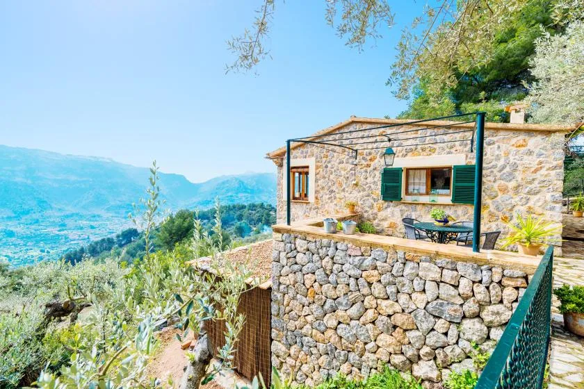 A stone house with a terrace overlooks a green valley.