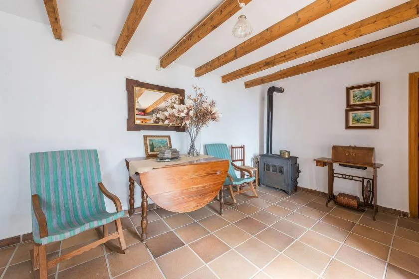 A rustic sitting room with wooden ceiling beams and a stove.
