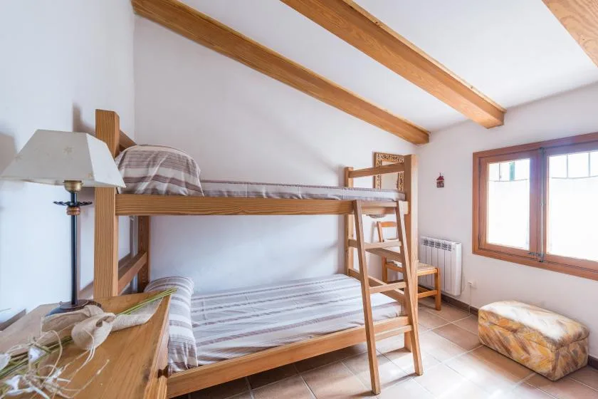 A bedroom with a wooden bunk bed, a window, and a small upholstered seat.