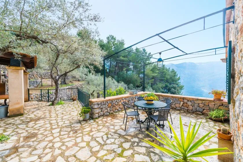 A stone-paved outdoor terrace has a dining table and mountain views.