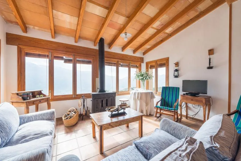 A bright living room with exposed wooden ceiling beams and large windows.