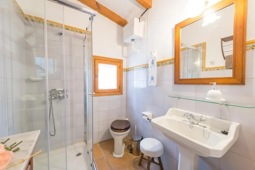 A tiled bathroom with a glass shower, toilet, and wall-mounted sink.