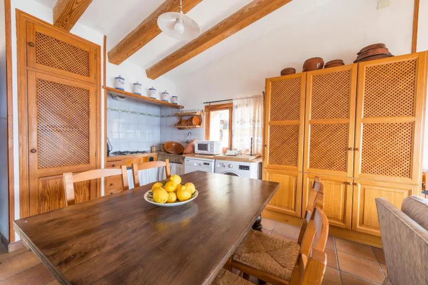 A dining area with a wooden table and chairs beside a tiled kitchen.