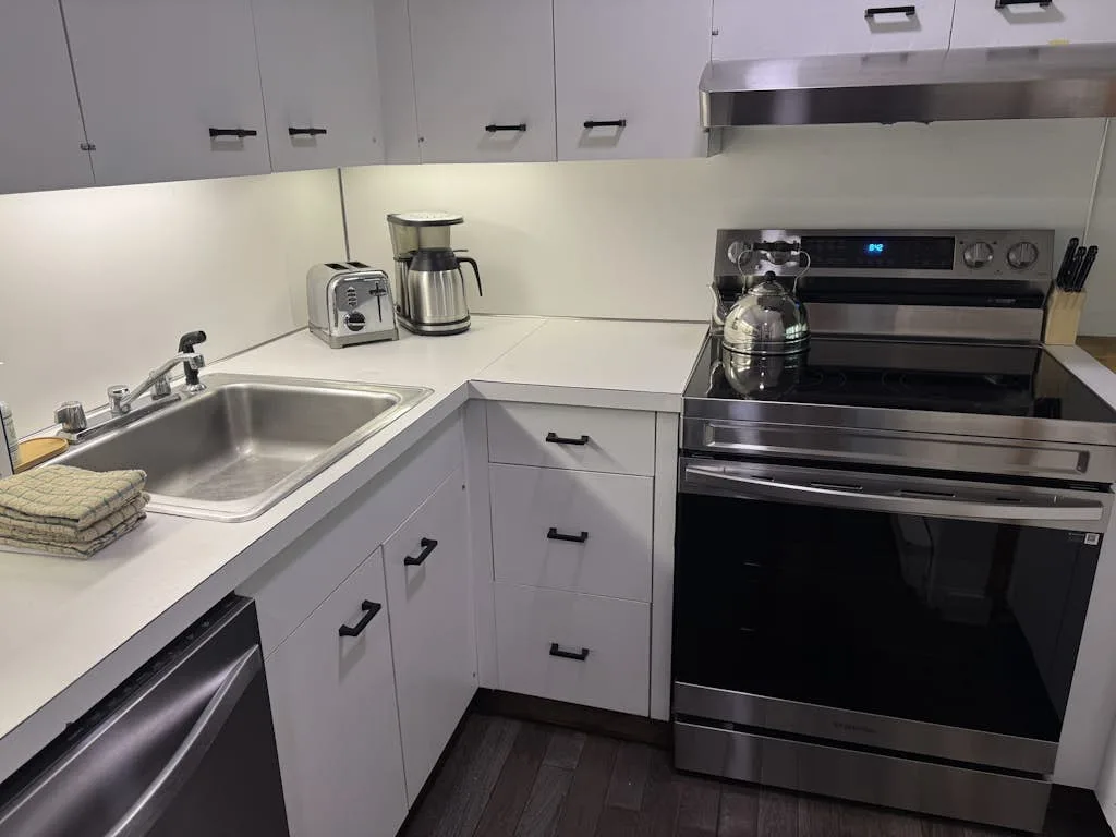 Una cocina luminosa con gabinetes blancos, un fregadero y un horno de acero inoxidable.