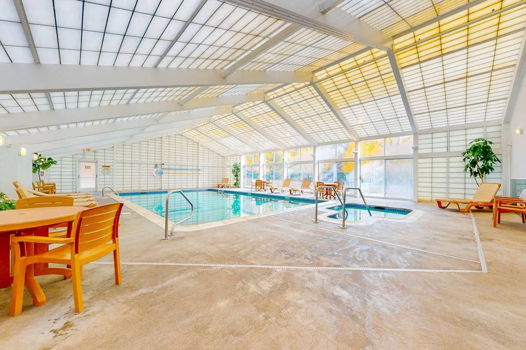 Una piscina cubierta está bajo un techo de vidrio luminoso, con asientos alrededor.