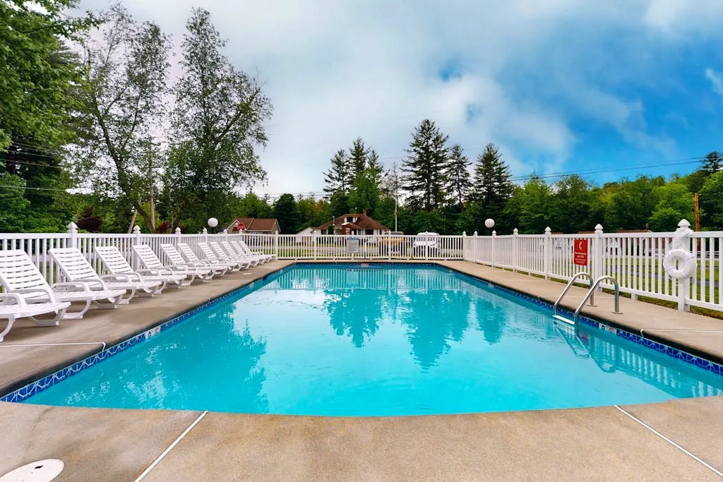 Piscina al aire libre rodeada de tumbonas blancas y una cerca blanca.