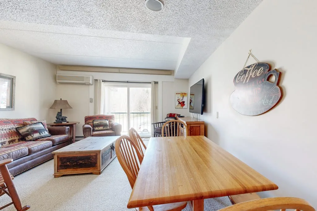 Una sala de estar y comedor con una mesa de madera, asientos y un televisor.