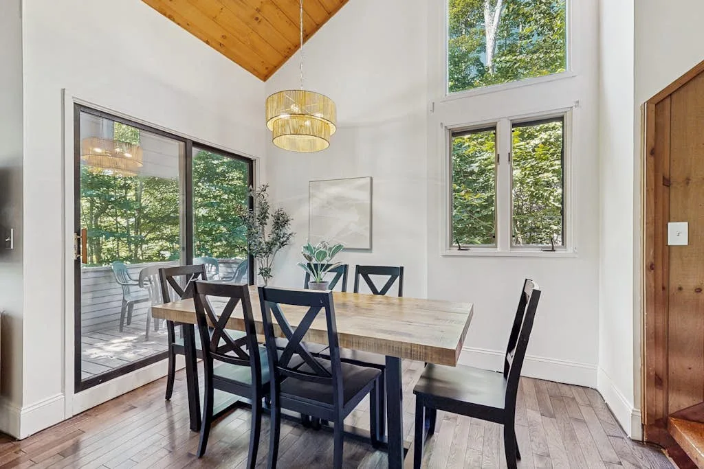 Un comedor con una mesa de madera y sillas junto a grandes ventanas.