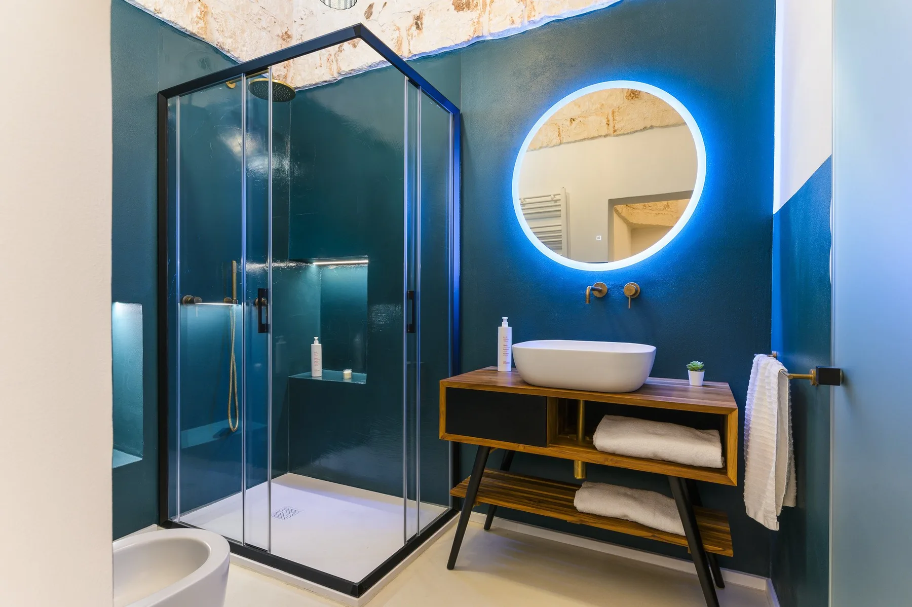 Un baño moderno con ducha de vidrio, tocador y espejo redondo iluminado.