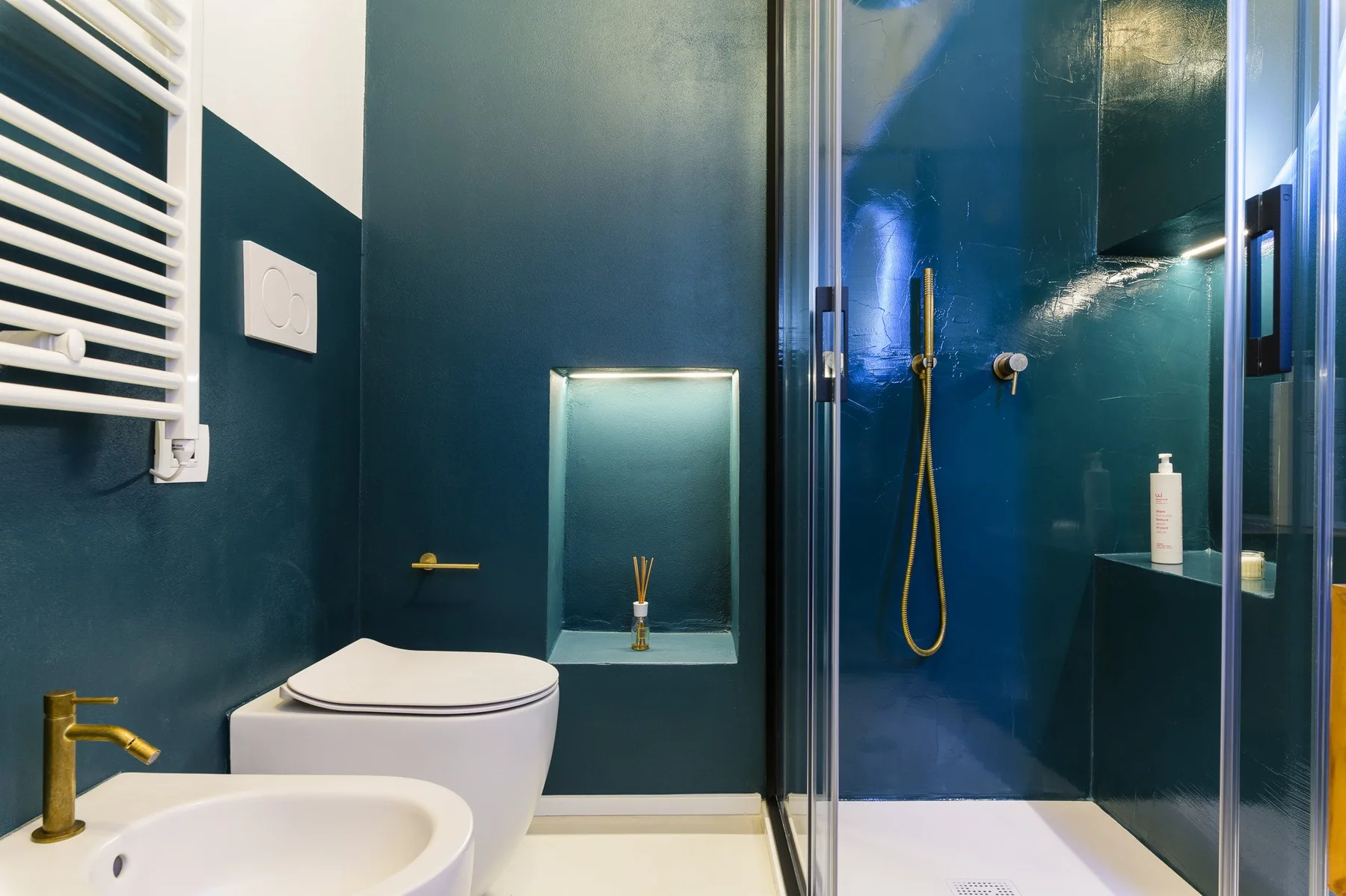 Un baño verde azulado oscuro con inodoro, lavabo y ducha con mampara de vidrio.
