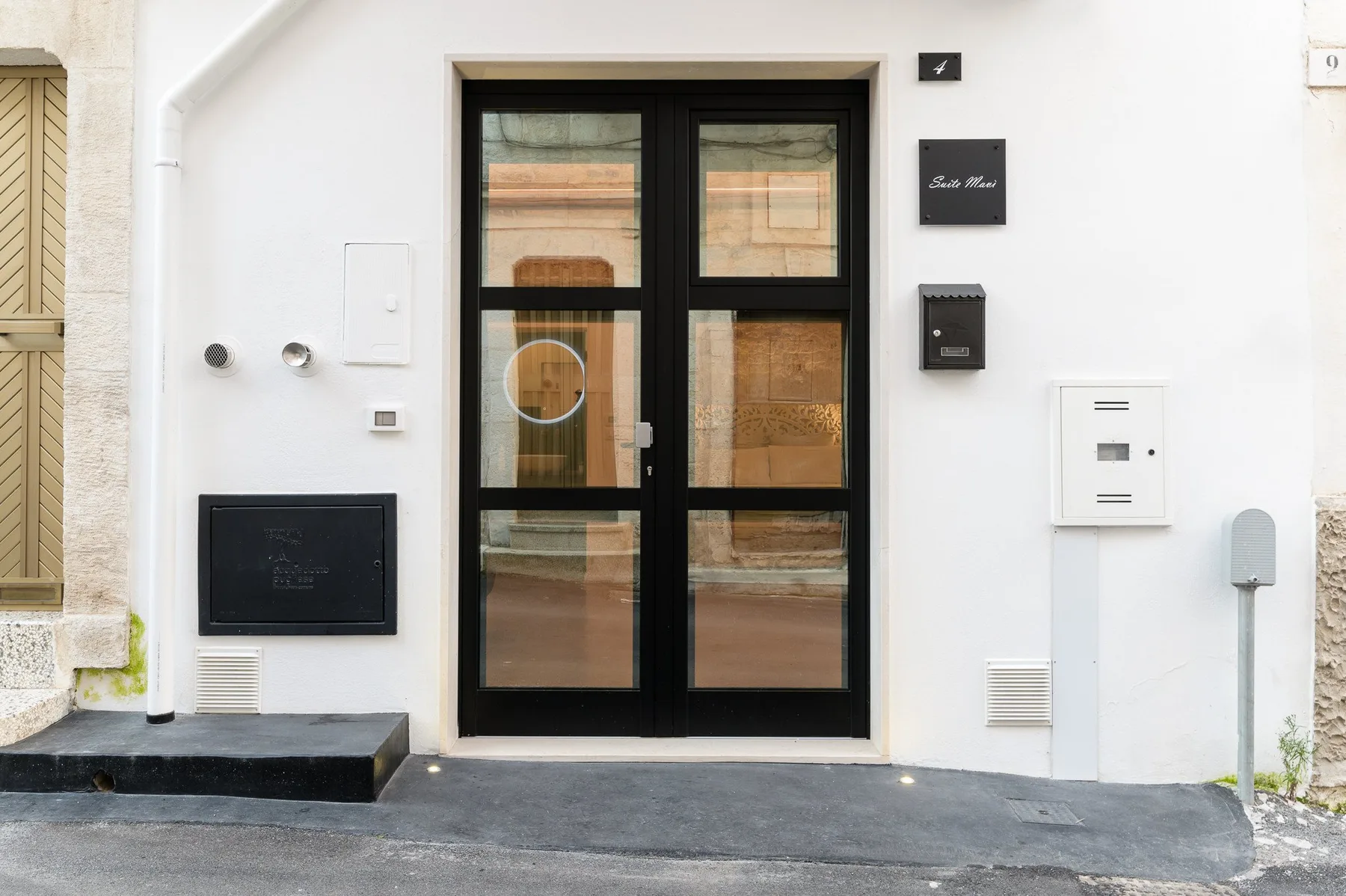 Entrada de un edificio a la calle, con puerta de vidrio de marco negro y paneles en la pared.
