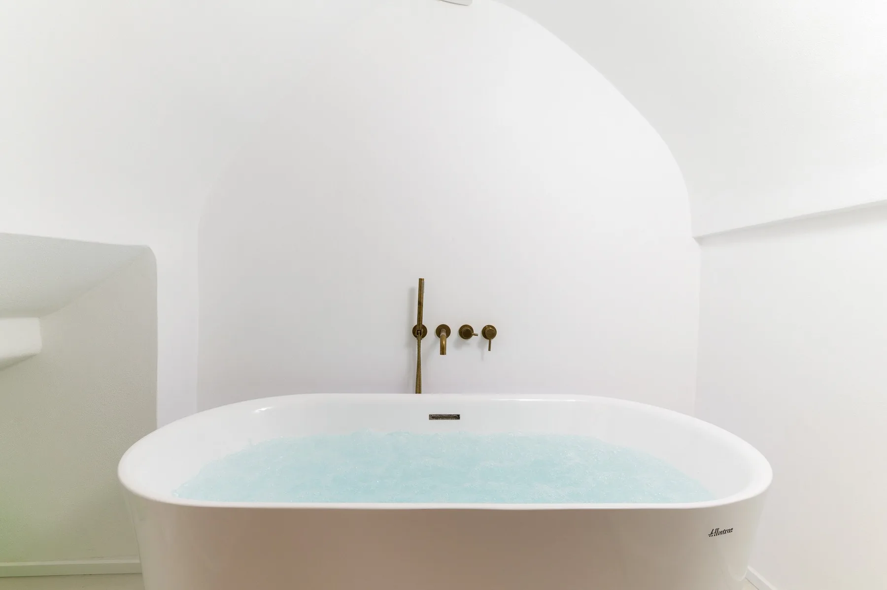Una bañera con agua azul claro está bajo unos grifos de pared de latón.