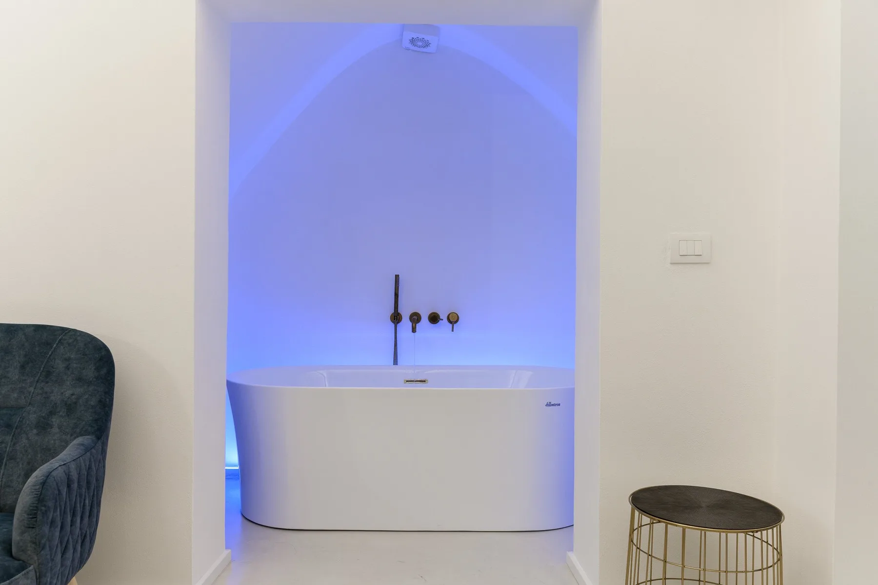 A freestanding bathtub sits in a recessed alcove with blue lighting.