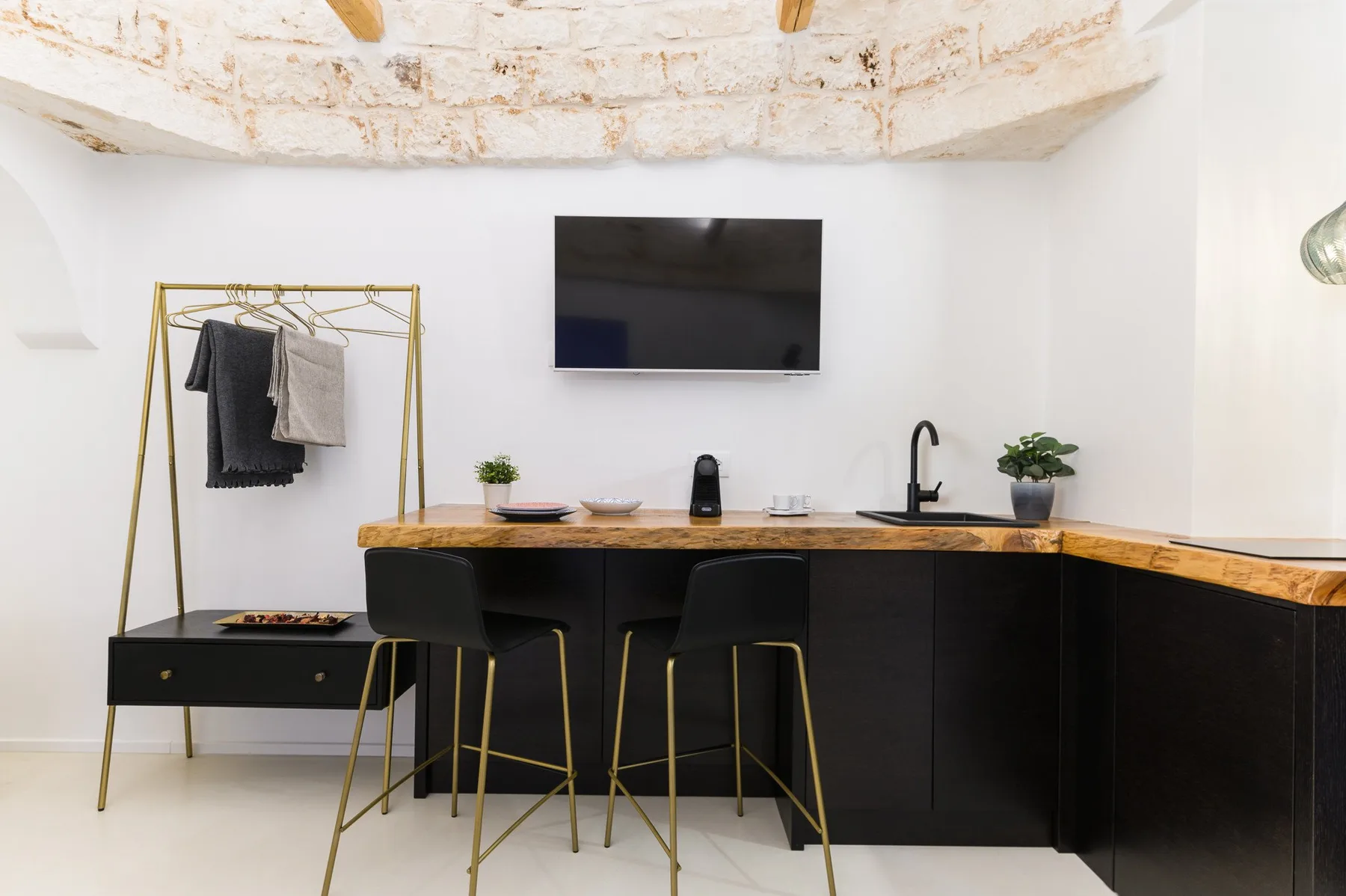 Una cocina con una encimera larga, asientos de bar y un televisor en la pared.