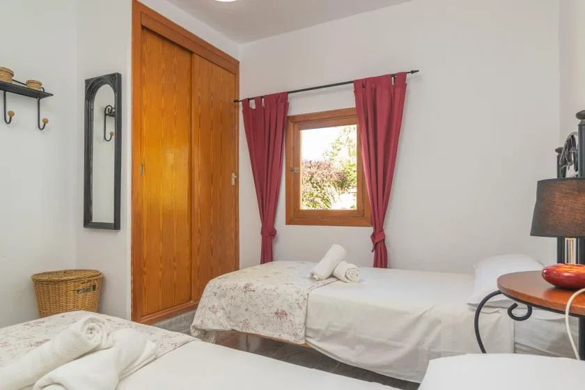 A bedroom with two beds and a window framed by red curtains.