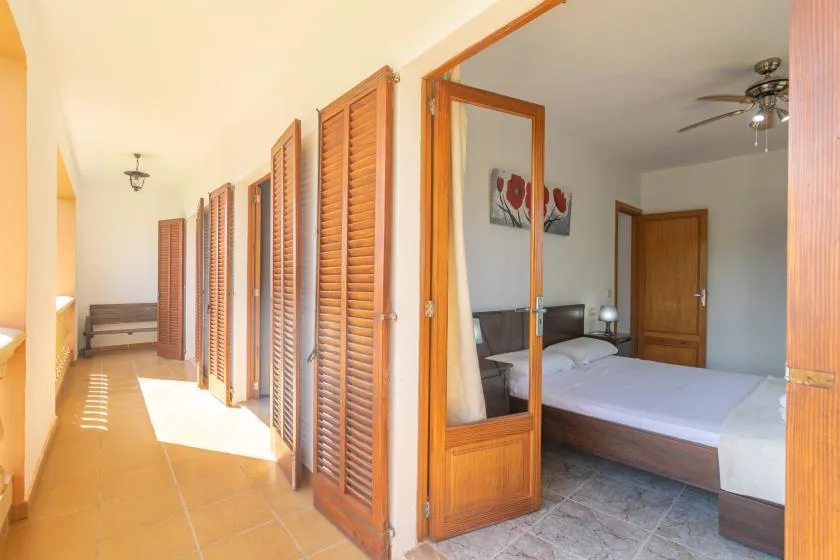 A bedroom with a bed is visible beside a hallway lined with wooden louvered doors.
