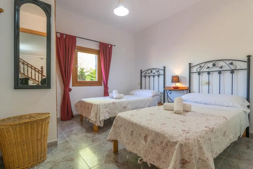 A bedroom with two beds, a window, and red curtains.
