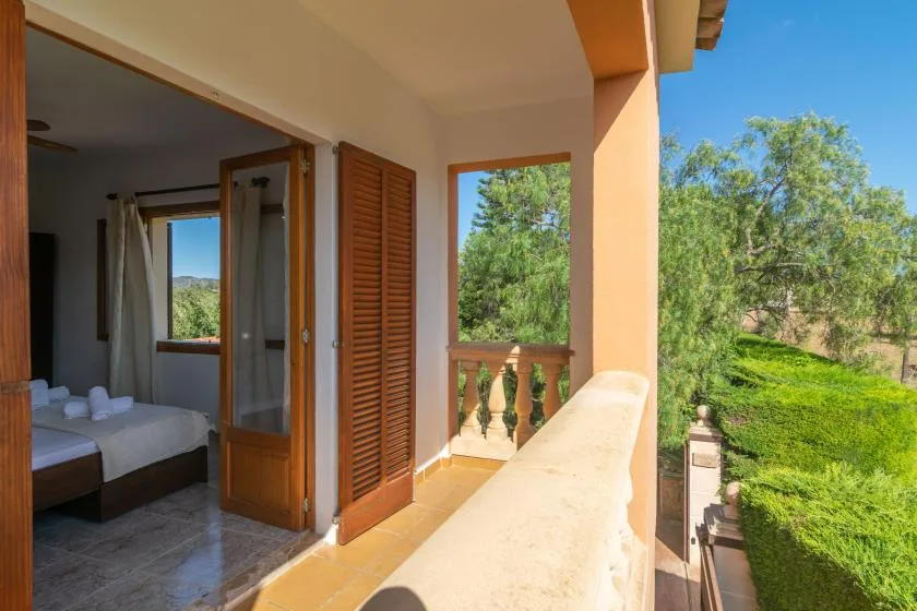 A covered balcony overlooks green trees and a garden.