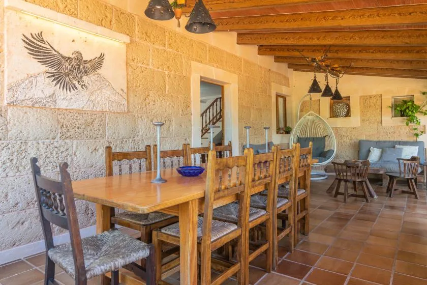 A dining area with a long wooden table and chairs beneath exposed ceiling beams.