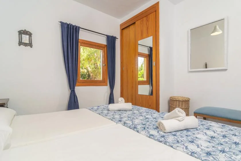 A bedroom with white bedding, blue patterned bedcover, and a wooden wardrobe.