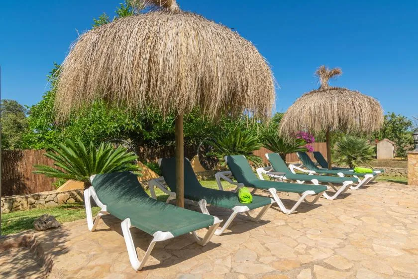 An outdoor poolside lounging area with reclining seats beneath thatched parasols.